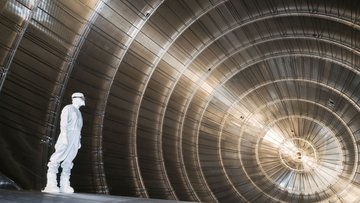 Ein in einem weißen Reinraumanzug gekleideter Wissenschaftler steht in einer sehr großen tunnelartigen Röhre