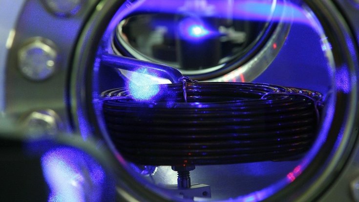 Blick in die Ultrahochvakuumkammer, in der Strontiumatome gekühlt und gespeichert werden | Bildquelle: Physikalisch-Technische Bundesanstalt Im oberen Drittel des Bildes ist das blaue Fluoreszenzlicht einer Wolke kalter Strontiumatome zu sehen – als tropfenförmiges Gebilde unter dem blau fluoreszierenden Atomstrahl