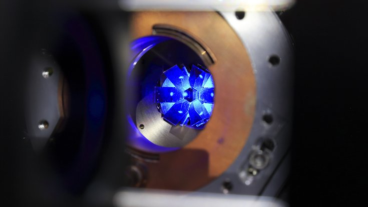 Floureszenz der Strontiumatome bei der Laserkühlung | Bildquelle: PTB Runde Öffnung von Metallteilen mit einem Leuchtpunkt in der Mitte und umgebendem Leuchten
