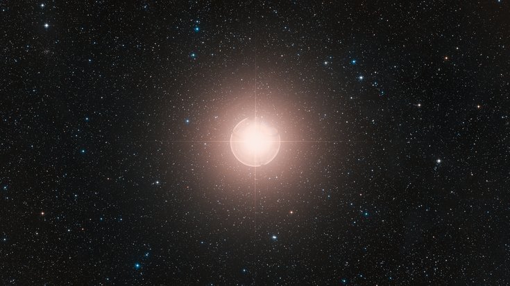 Stern Beteigeuze | Bildquelle: ESO/Digitized Sky Survey 2. Acknowledgment: Davide De Martin. Im Zentrum der Aufnahme befindet sich der hell leuchtende Stern Beteigeuze. Um ihn herum befinden sich viele kleine Lichtpunkte.